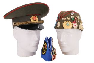 A Soviet army peaked cap together with two caps having numerous badges affixed