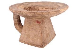 An African carved wooden stool, having a dished circular top and truncated pyramidal base with