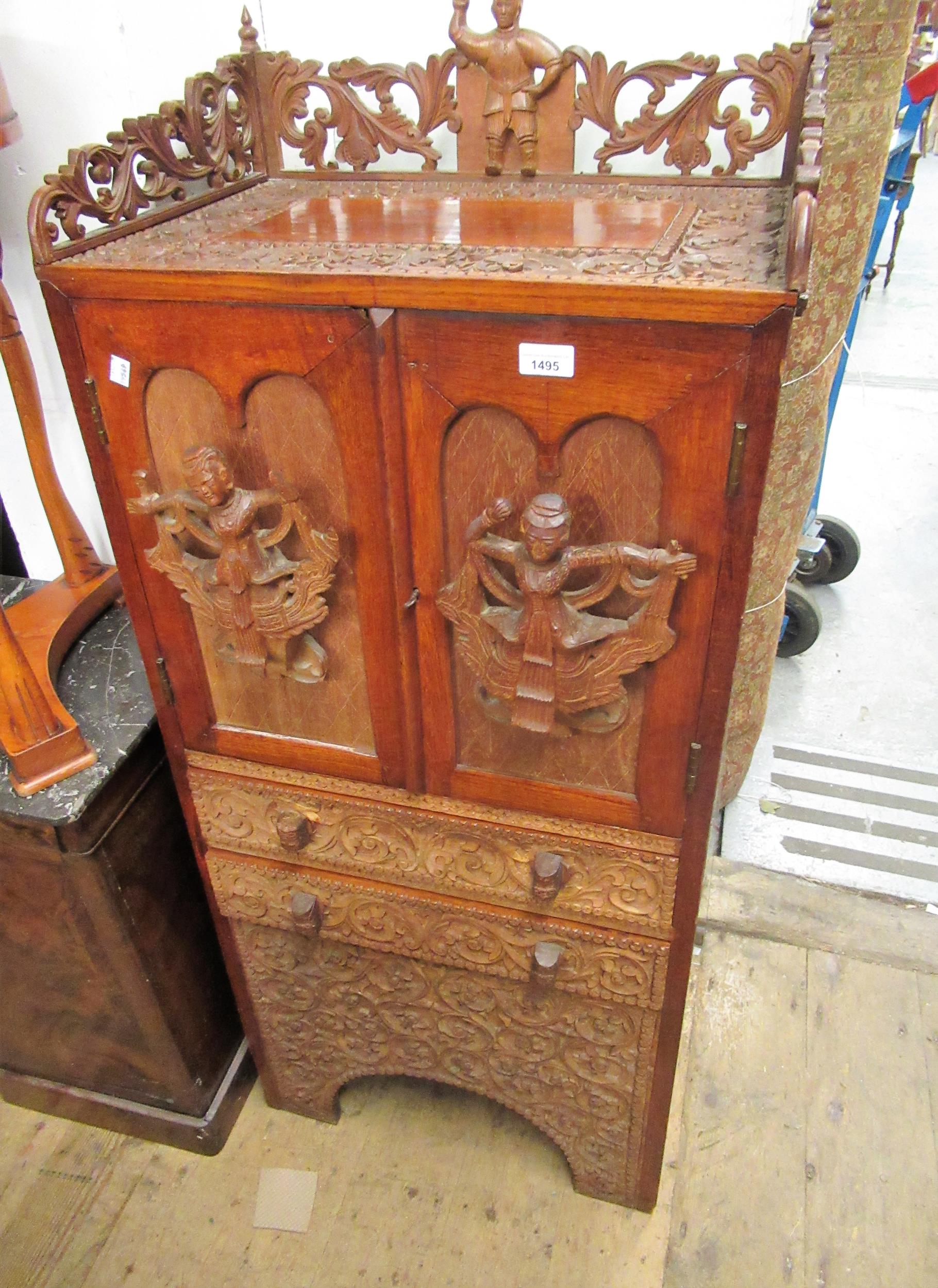 Burmese carved hardwood narrow side cabinet, the galleried top above two doors, with applied figural