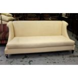 Andrew Martin, three seat wing arm sofa, covered in a cream woven fabric, raised on low square