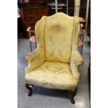 Gold damask upholstered wingback armchair, raised on mahogany carved cabriole and pad supports (at