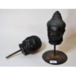 Brown patinated metal buddha head on a circular stand together with another similar