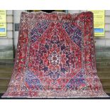 A PERSIAN RUG, 20TH CENTURY, THE RECTANGULAR FIELD CENTRED WITH A LARGE OPEN STYLISED FLOWER
