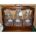 A MAHOGANY TANTALUS WITH THREE GLASS DECANTERS AND STOPPERS, WITH THREE PORCELAIN SPIRIT LABELS - '