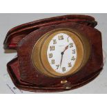AN ART DECO LEATHER CASED TRAVELLING CLOCK, THE GILT METAL CLOCK WITH OVAL ENAMEL DIAL BEARING