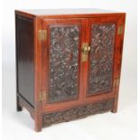 A Chinese dark wood side cabinet, the panelled rectangular top above a pair of cupboard doors carved