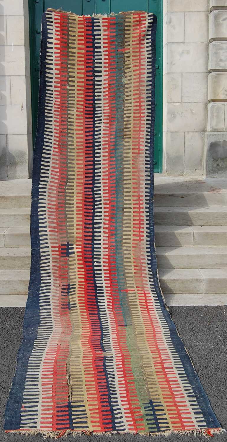 A blue ground kelim runner, decorated with rows of off-white, madder, ochre and green teeth shaped