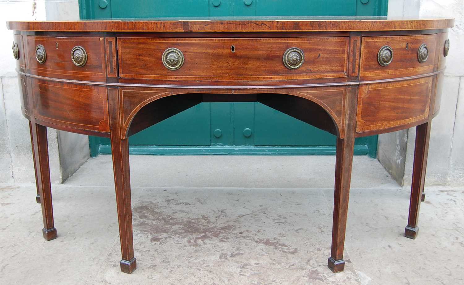 A George III mahogany and boxwood lined demi lune sideboard, the shaped top with fan-shaped line