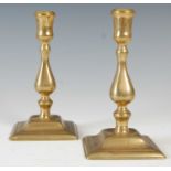 A pair of antique brass candlesticks, the baluster shaped stems mounted on square plinth bases, 17cm