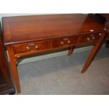 A reproduction side table with three rectangular pull-out drawers with brass handles, raised on four