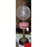 A Victorian paraffin lamp with pink glass font raised on a brass column to a black circular base,