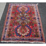 A small Persian rug, the madder ground centred with Art Nouveau stylised medallion of flowers and