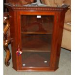 An early 20th century mahogany hanging corner cupboard with dentil frieze