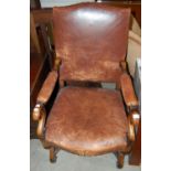 An early 20th century brown leather upholstered beechwood elbow chair with inverted scroll supports