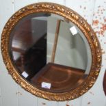 A gold coloured circular wall mirror with carved foliate detail and bevelled glass plate