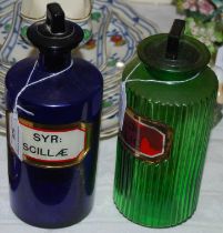 Two vintage apothecary glass jars, one blue with label 'SYR: SCILLAE', the other in green glass with