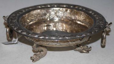 An Eastern white metal twin handled bowl, raised on three mythical fish supports with embossed