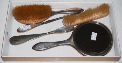 A five-piece silver mounted dressing table set comprising handheld mirror, two brushes, boot hook