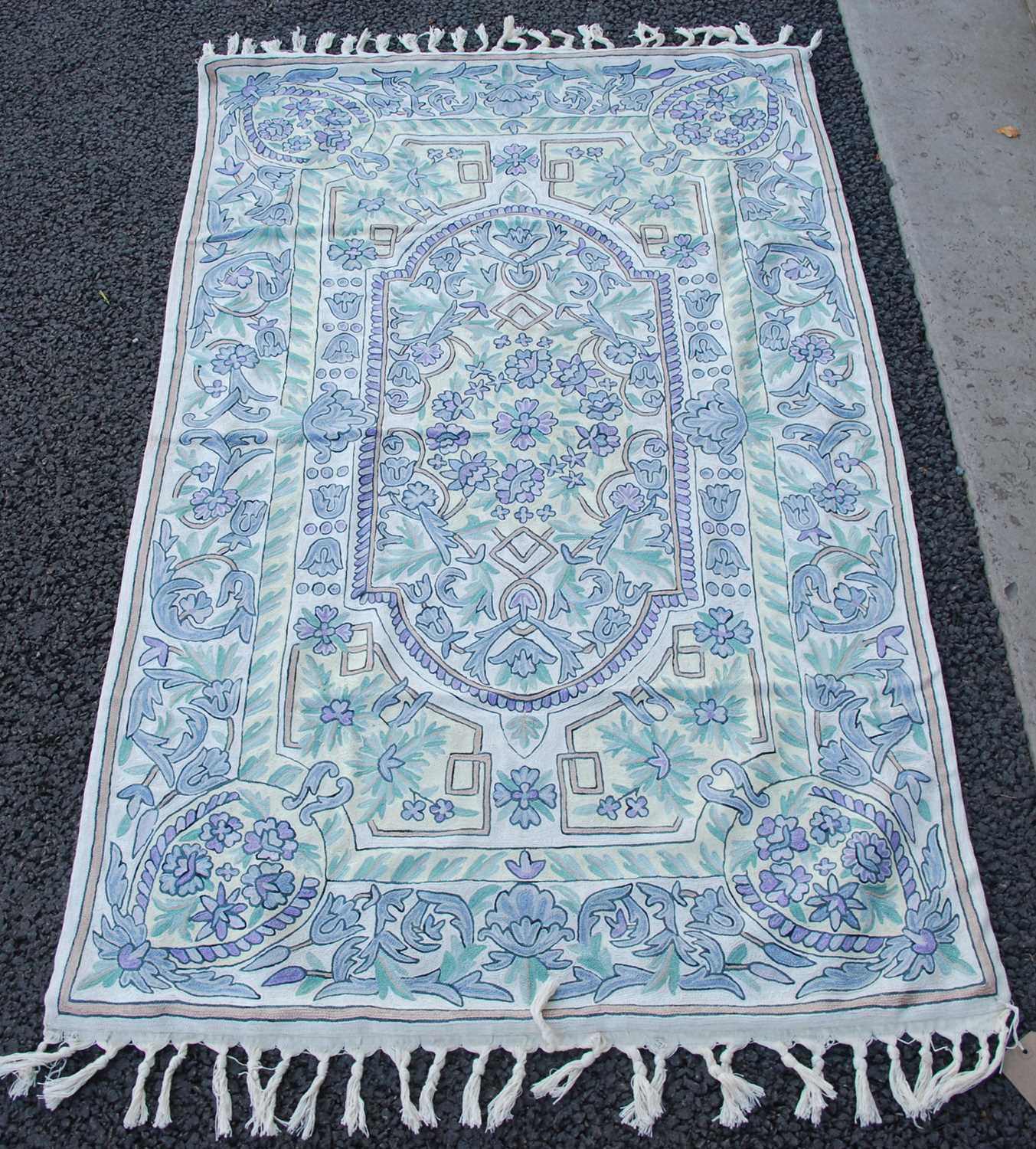 A white ground tasseled rug with repeating borders of stylised flowers in shades of purple and