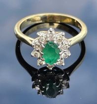 An 18ct gold, emerald and diamond cluster ring, centred with an oval facet cut emerald, calculated