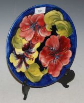 A Moorcroft pottery plate, decorated with hibiscus on a blue ground, impressed marks, green