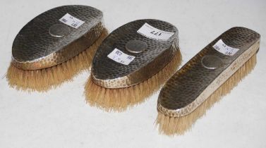 A silver backed three piece brush set with London hallmarks and hammered finish, oval shaped initial