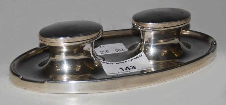 An early 20th century silver oval shaped desk stand with two hinged inkwells, lacking liners,