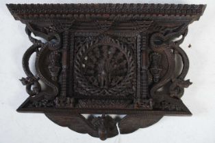 An Indonesian carved wooden wall plaque centred with a peacock flanked by deities and dragons, of