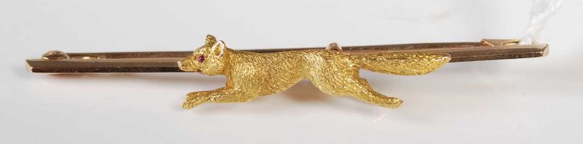 An early 20th century yellow metal bar brooch, set with a running fox, stamped '15ct' with two