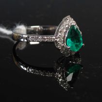 A white metal, emerald and diamond cluster ring with diamond set shoulders, set with one pear-shaped