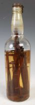A bottle containing treen carved farm working implements, soaked in a clear solution.