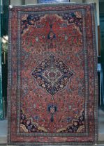 A Persian rug, early 20th century, the abrashed madder rectangular field centred with a blue