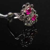 A white metal, ruby and diamond set flower ring, set with two oval faceted rubies and seven round