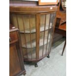 An early 20th century walnut veneered bow front glazed cabinet on ball and claw feet