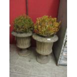 A pair of composite stone garden urns with reeded bodies and plants