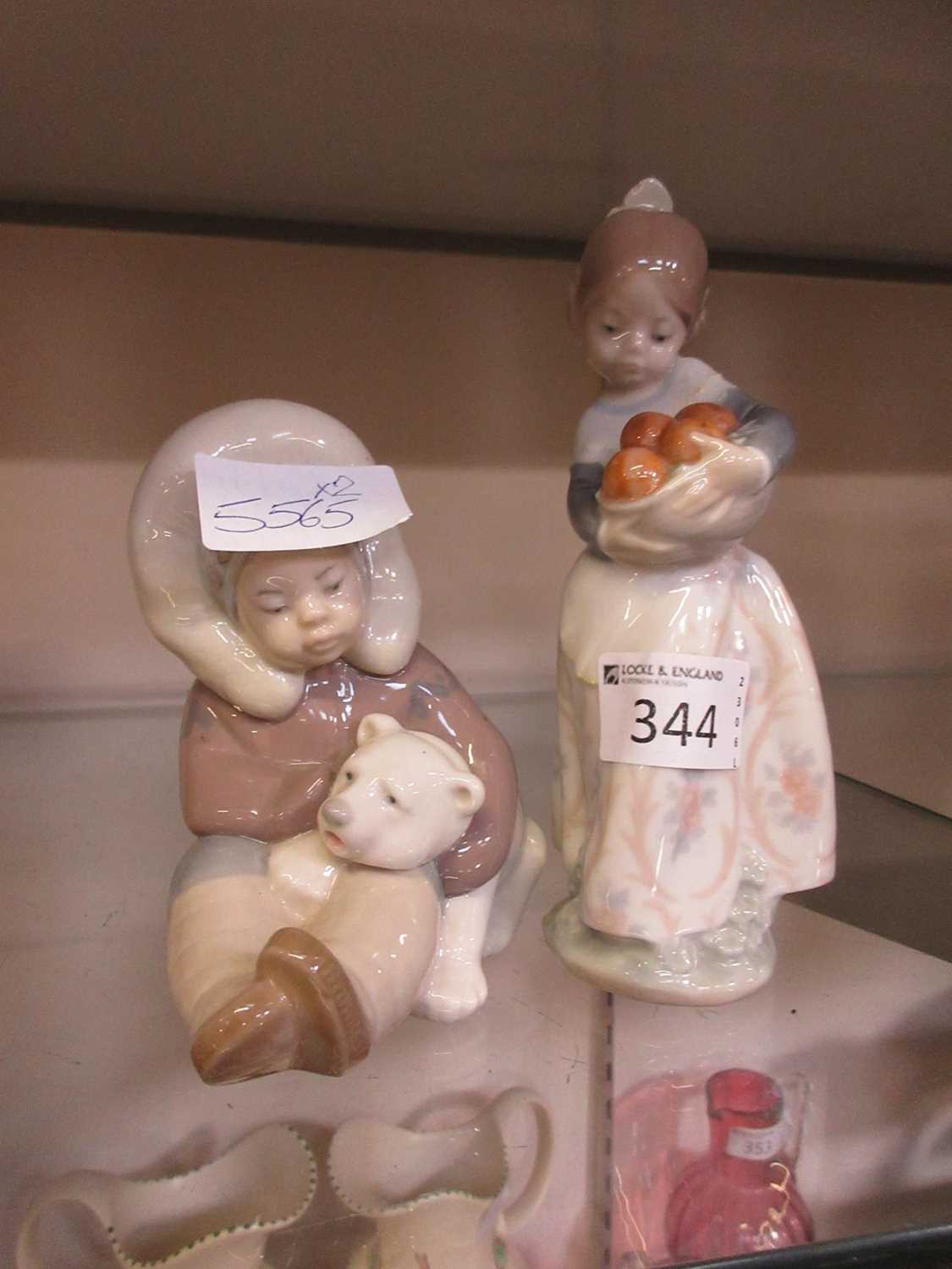 Two Lladro figurines, one a child with a polar bear cub, the other a girl with oranges