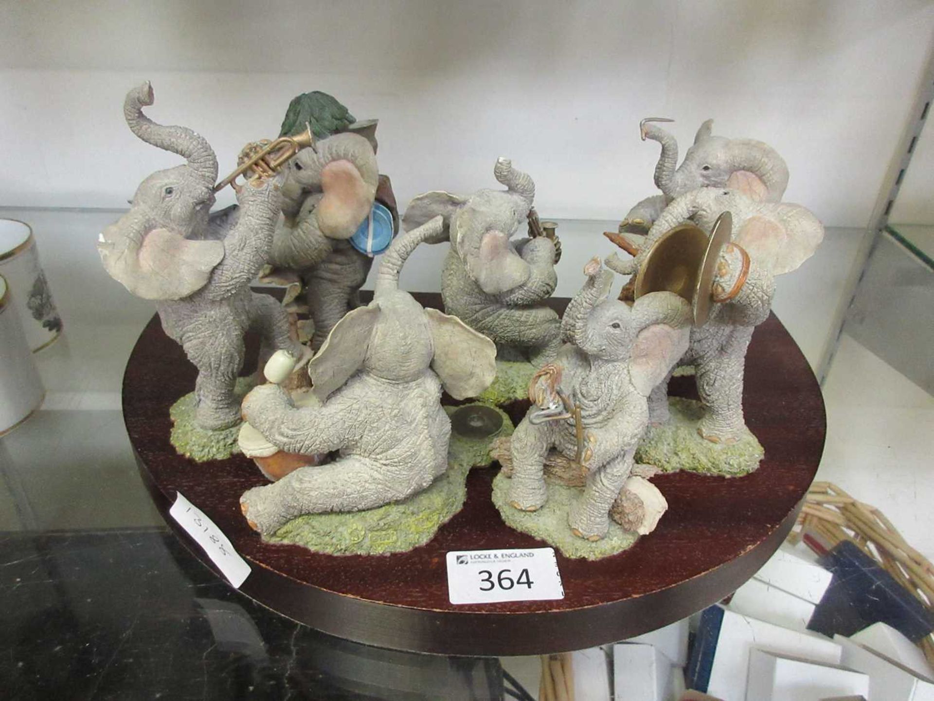 An assortment of seven moulded figurines of elephants playing instruments on a wooden base