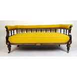 An Edwardian ebonised, parcel gilt and brass mounted settee upholstered in a yellow fabric, the