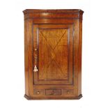 An 18th century oak and inlaid wall hanging corner cupboard, the single blind panel door over two