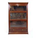 An early 20th century walnut sectional bookcase, comprising of plinth, base section with drawer
