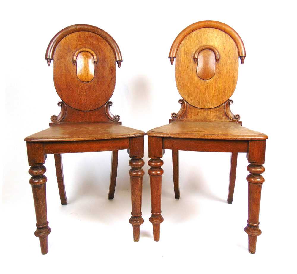 A pair of 19th century oak hall chairs, the oval back supported on carved C-scrolls on turned