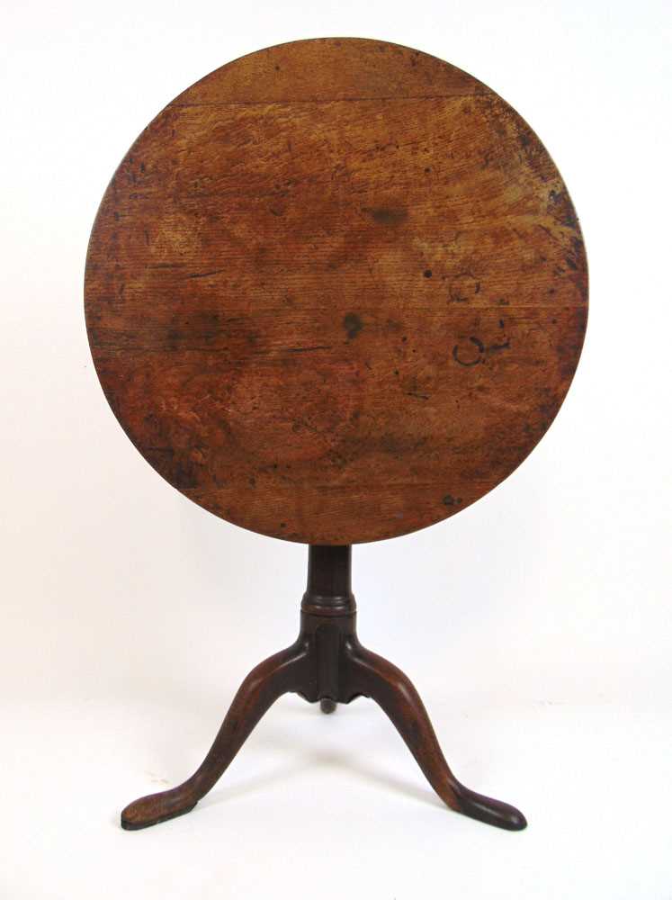 An 18th century oak tilt top tripod table, the circular top on a turned column on three splay