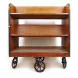 An early 20th century oak library trolley, two angled bookshelves over open storage on four castor