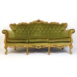 A reproduction giltwood three seat sofa in the baroque style upholstered in a cut green button