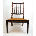 An early 19th century rosewood nursing chair, the bobbin turned spindle back over the caned seat