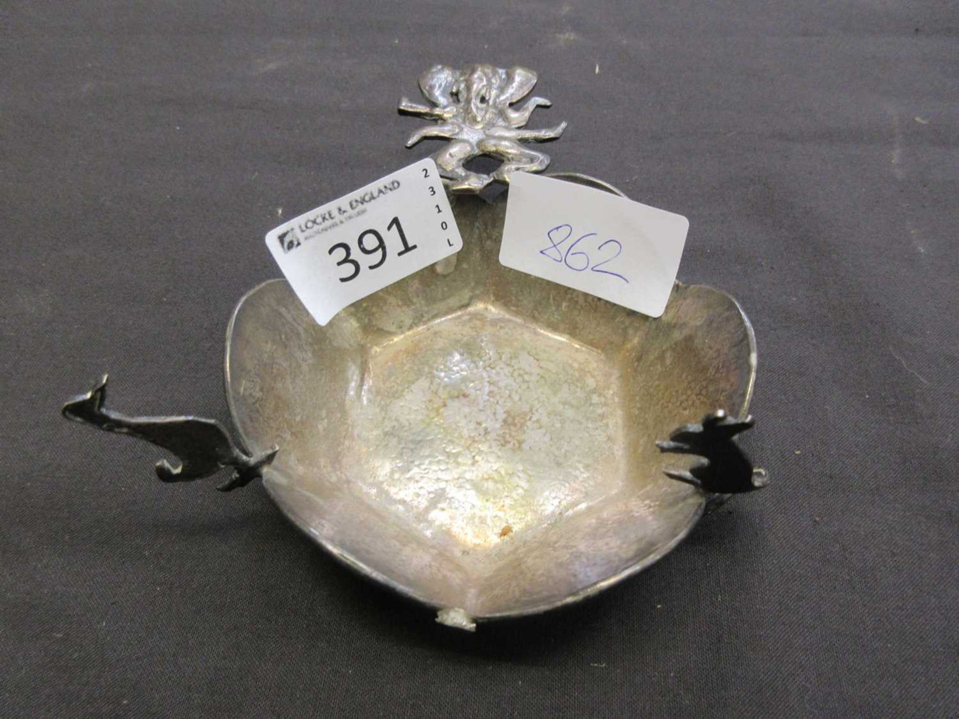 A hammered white metal pin dish with duck, rat, and elephant design