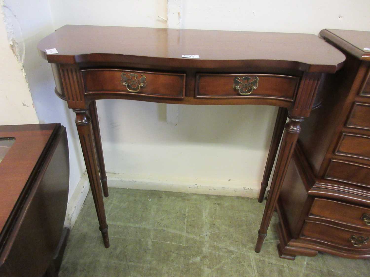 A reproduction mahogany serpentine fronted side table with two drawers on fluted legs