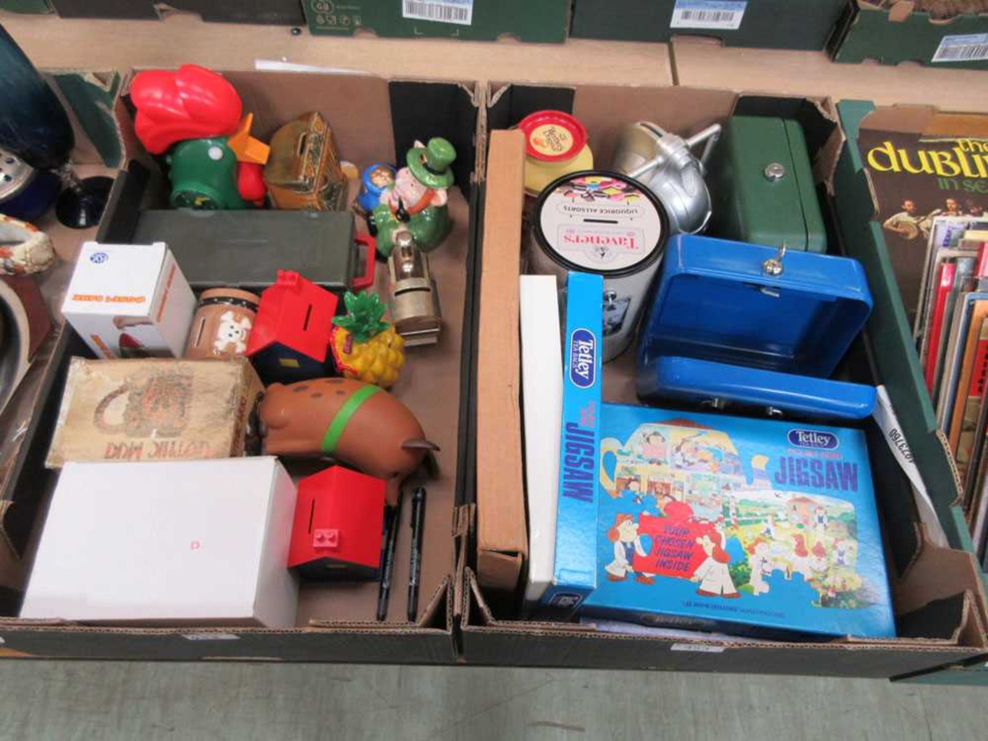 Two trays of modern Tetley and other related items to include jigsaws, lockable cash tins, etc