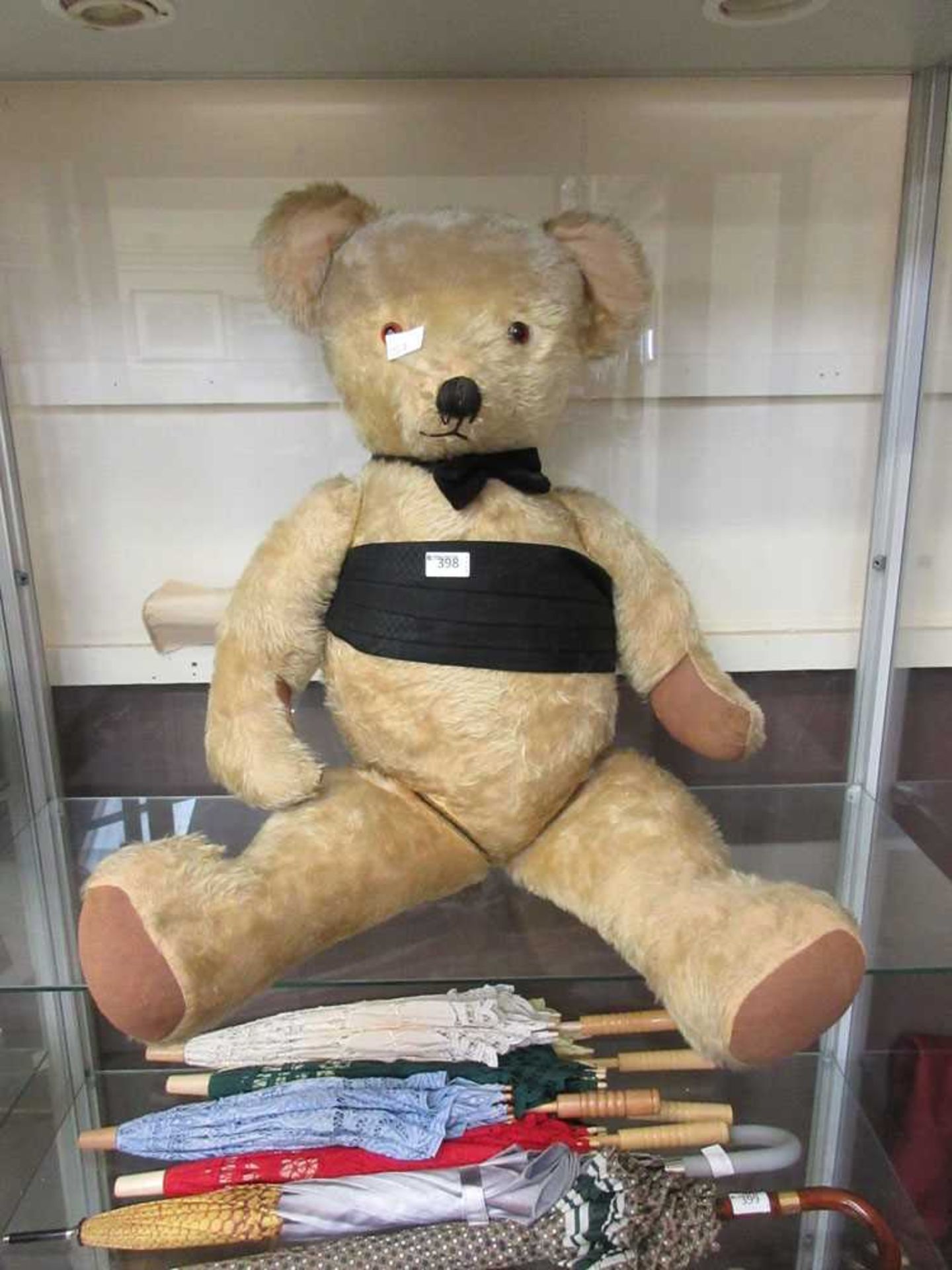 An early 20th century jointed teddy bear with black sash and bow tie94cm tall.