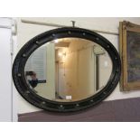 An early 20th century black framed oval bevel glass mirror with brass spheres
